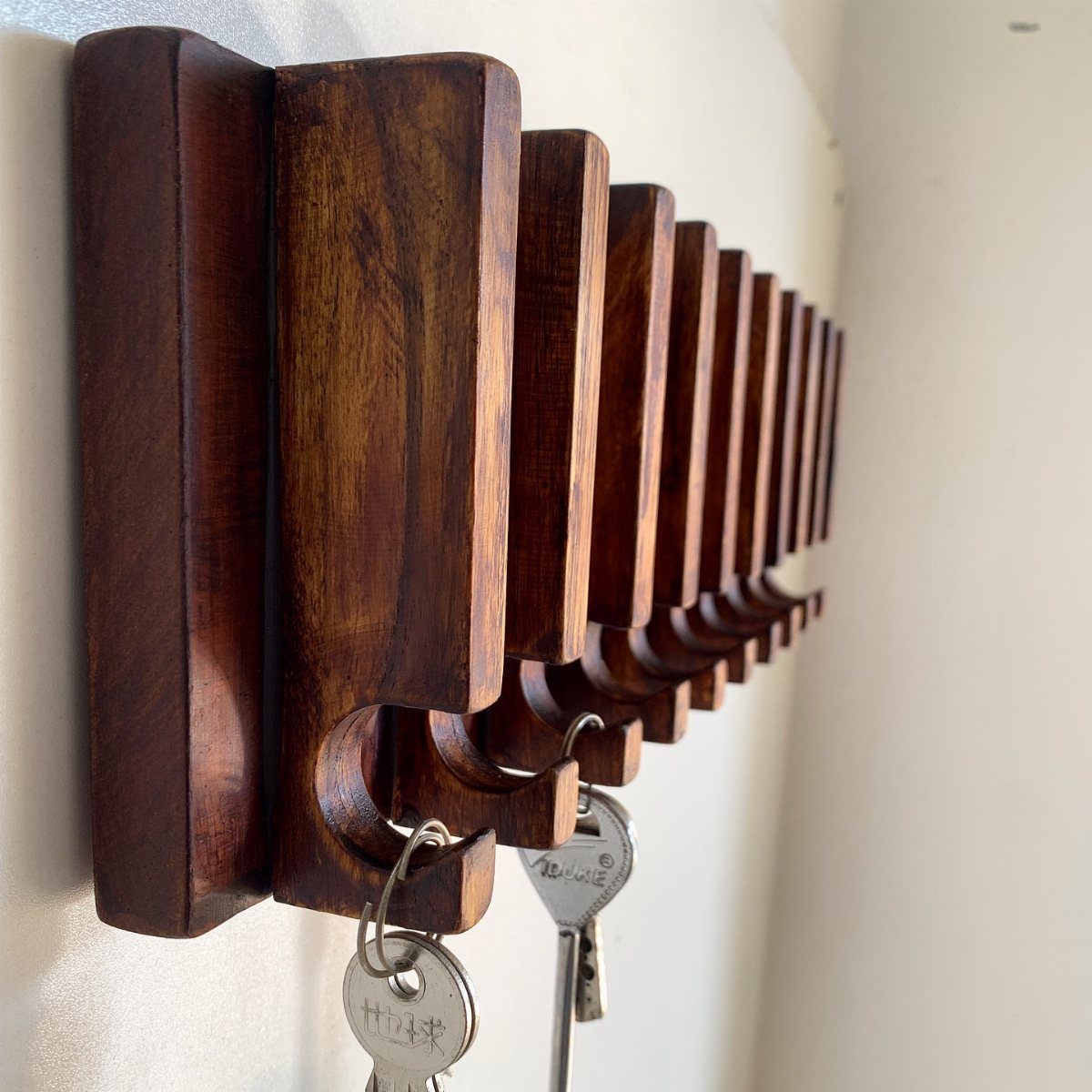 Wooden key holder with multiple slots holding silver keys on a white wall.