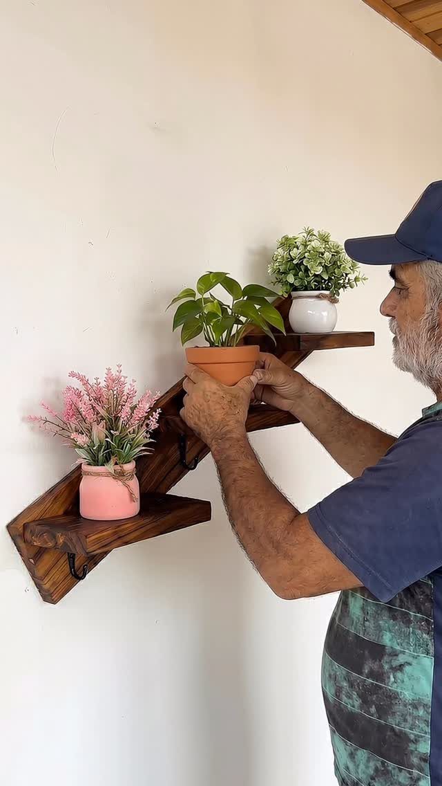 Wooden wall-mounted shelf with hooks holding small potted plants and a man's hands.